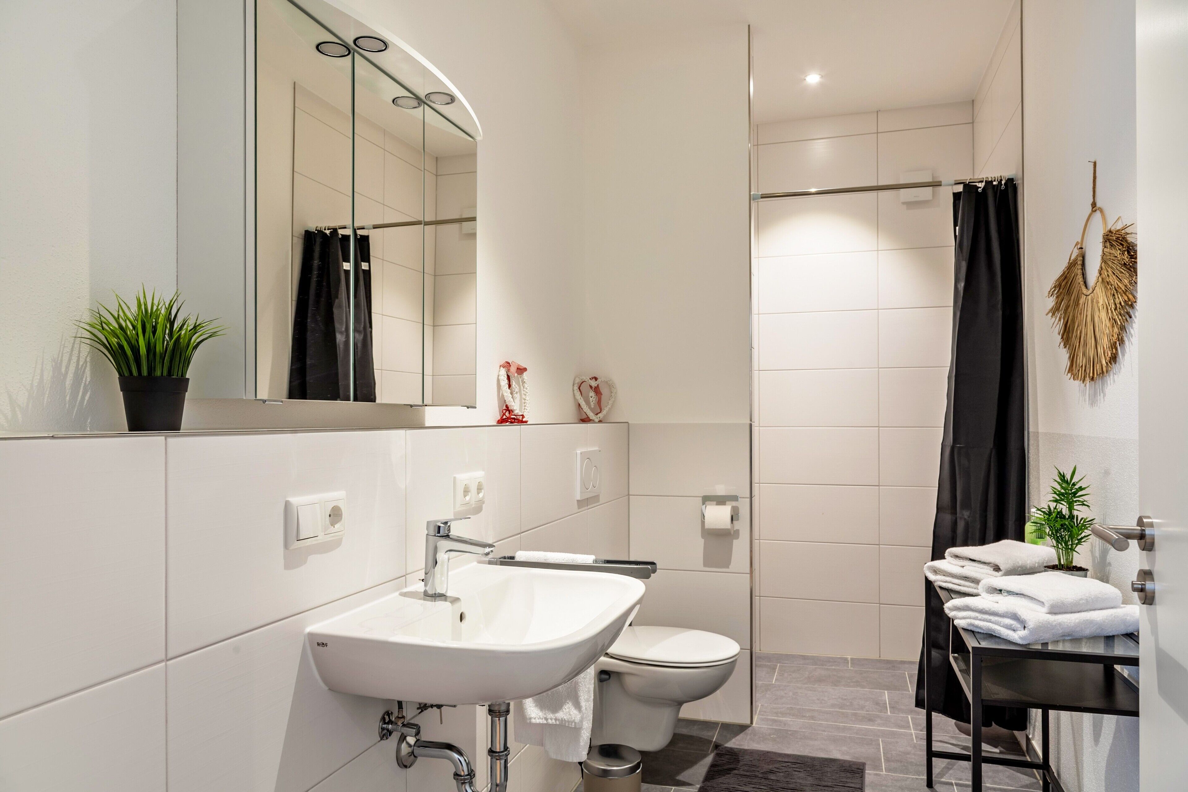 Un baño moderno con lavamanos, espejo, inodoro y ducha.