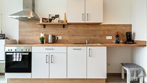 A modern kitchen with white cabinets, a stainless steel range hood, a wooden countertop, and a built-in oven.