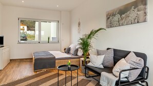 A modern, well-lit room with a bed, a sofa, a small table, and a large window.