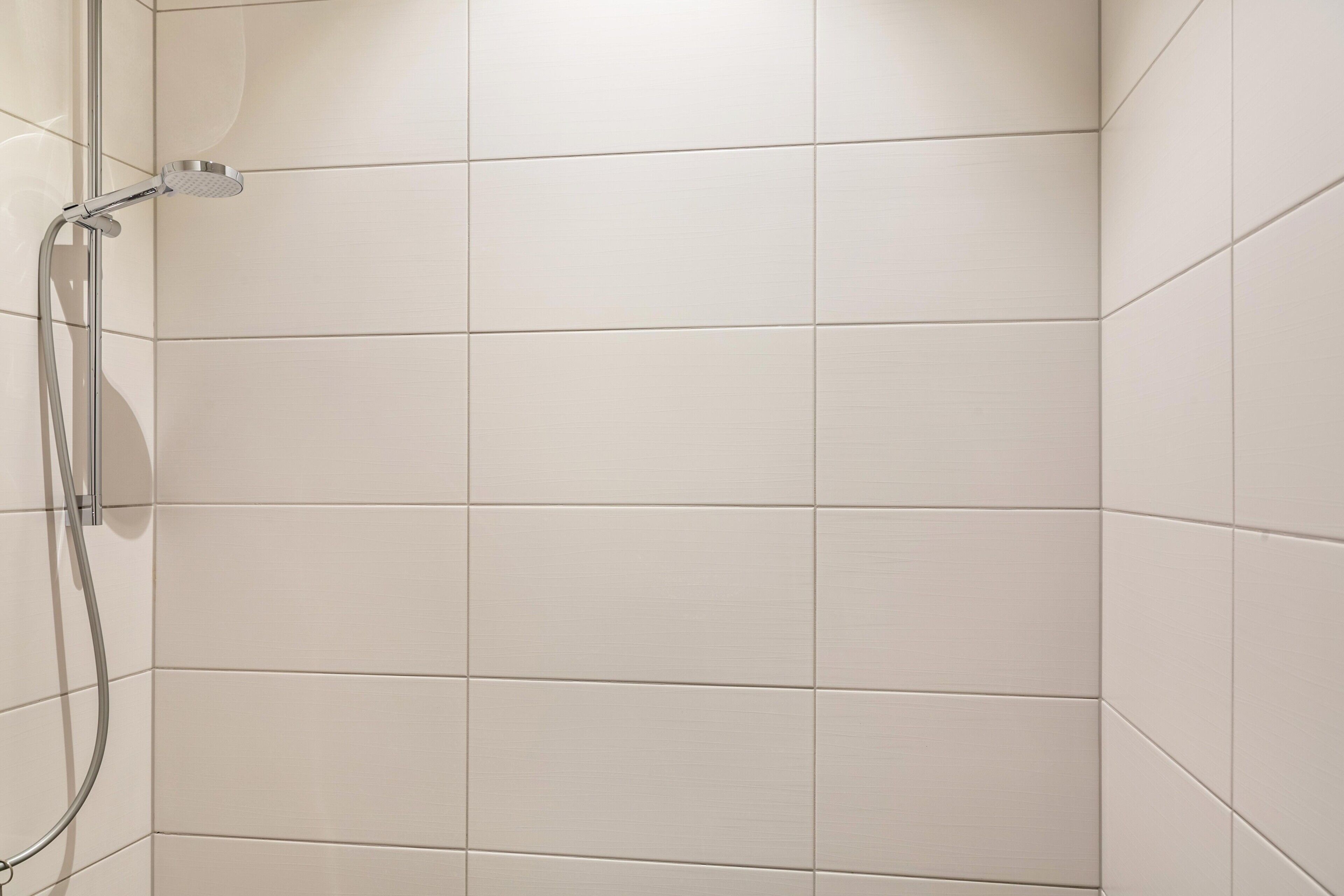 A shower area with white tiles and a chrome showerhead.