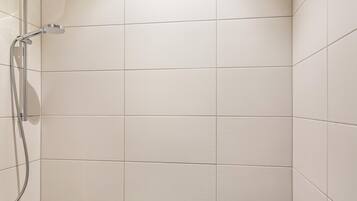 A shower area with white tiles and a chrome showerhead.