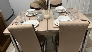 Ein Esszimmer mit Tisch, Tellern, Schüsseln und Gläsern, umgeben von Stühlen mit strukturierter Oberfläche.