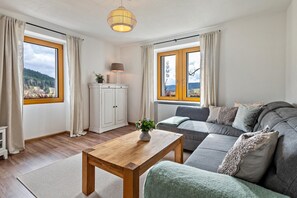 A modern living room with a sofa, a wooden coffee table, a cabinet, and large windows with curtains. - Holiday Apartment "Haus Bergruh Kuckucksnest" with Mountain View, Shared Terrace & Wi-Fi (Todtnauberg)