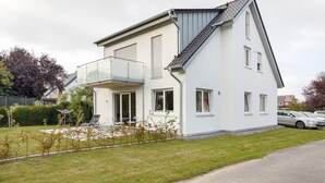 A modern two-story house with a balcony, a driveway, and a parking area.