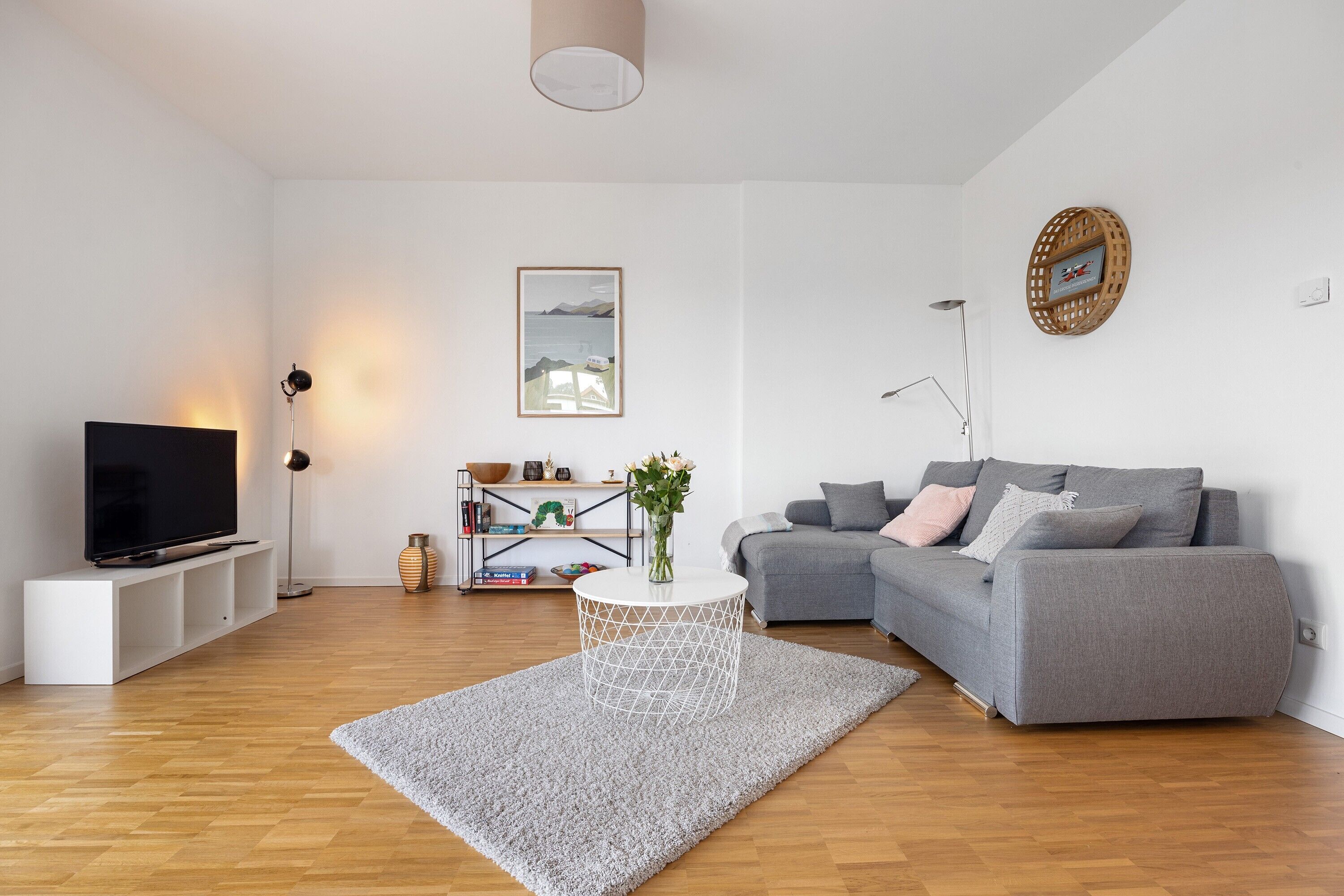 Un salon moderne avec un téléviseur à écran plat, un canapé gris, une table basse blanche et une bibliothèque.