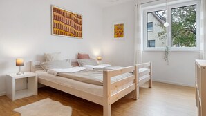 A bedroom with a wooden bed, white nightstands, a white rug, and two wall-mounted lamps.