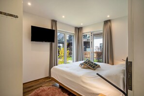 Un dormitorio con cama, televisión montada en la pared y ventana con cortinas.