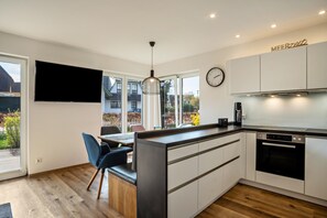 A modern kitchen with a built-in island, a flat-screen TV, and a clock on the wall. - Apartment 'Wohnung Strandperle' with Private Terrace, Private Garden and Wi-Fi (Zingst)