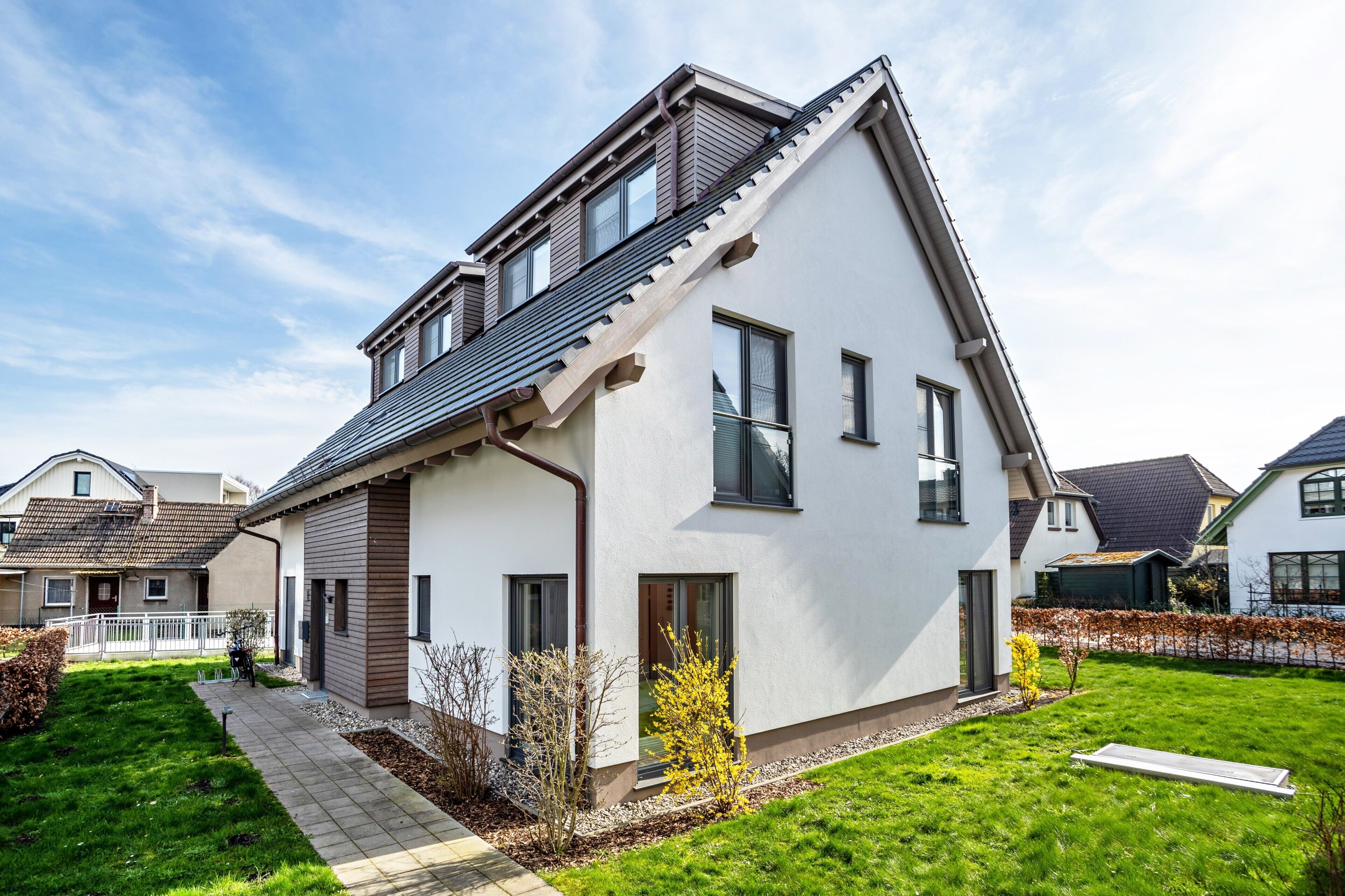 Ett modernt hus i två våningar med ett sluttande tak, stora fönster och en välskött gräsmatta.
