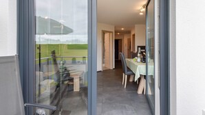 A modern interior with a balcony, a dining area with a table and chairs, and a view of a green landscape. - Apartment 'Schwarzwaldpanorama, 76qm' with Mountain View, Shared Terrace and Wi-Fi (Höchenschwand)