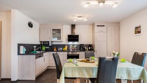 A modern kitchen with a dining area, featuring a microwave, stove, and cabinets. - Apartment 'Schwarzwaldpanorama, 76qm' with Mountain View, Shared Terrace and Wi-Fi (Höchenschwand)