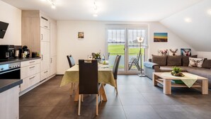 A modern kitchen with a dining area, a sofa, and a view of a green landscape through large windows. - Apartment 'Schwarzwaldpanorama, 76qm' with Mountain View, Shared Terrace and Wi-Fi (Höchenschwand)