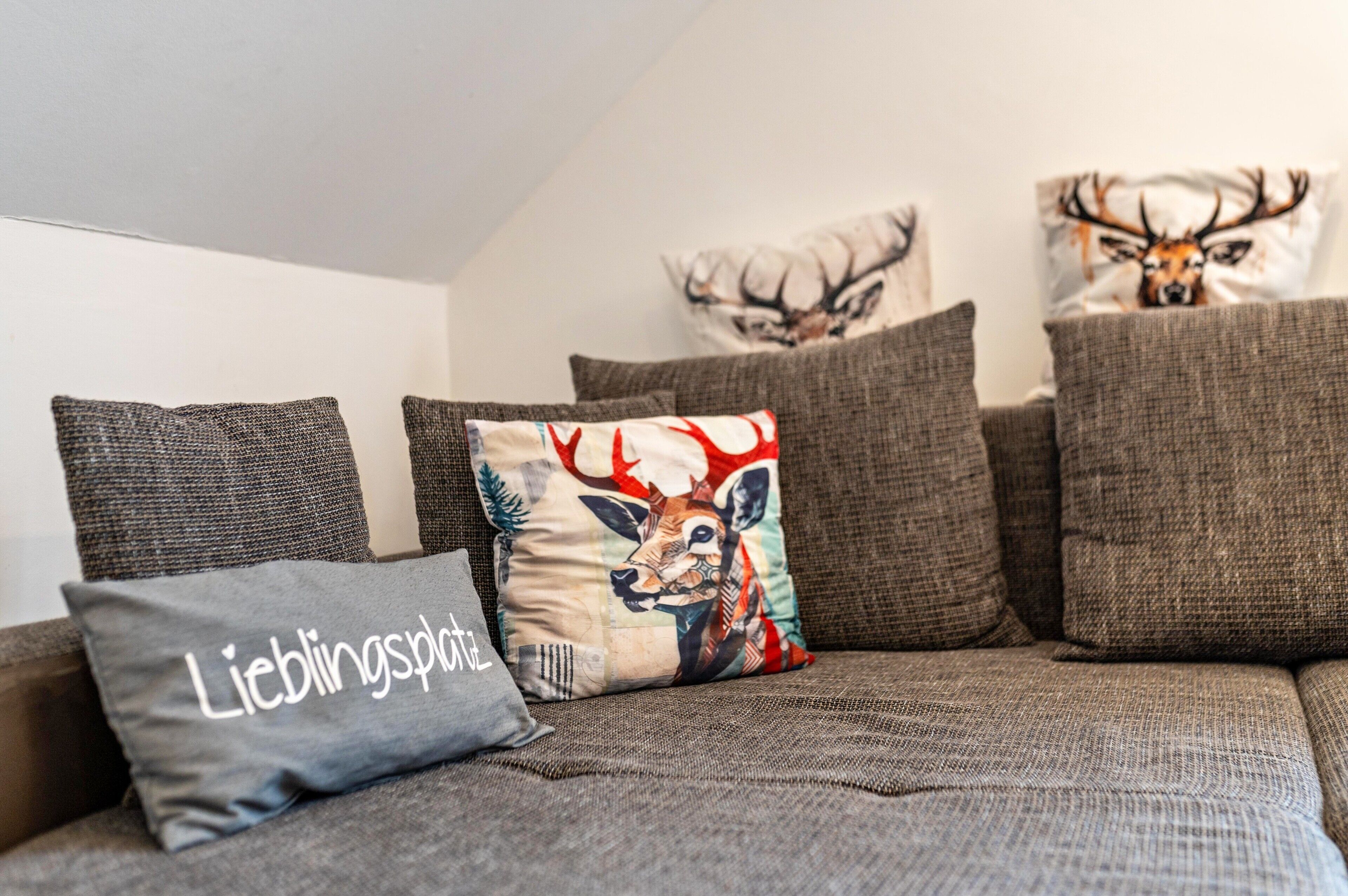 Ein Sofa mit mehreren Kissen, eines mit einem Hirschmotiv und das andere mit einem Hirsch und Geweihen.