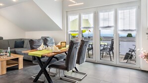 Un salon moderne avec un coin repas, de grandes fenêtres et une vue sur la mer.