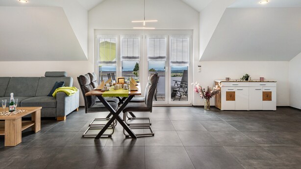 Un appartement moderne de style «loft», comprenant un coin repas, un canapé, une cuisine et de grandes fenêtres offrant une vue dégagée.