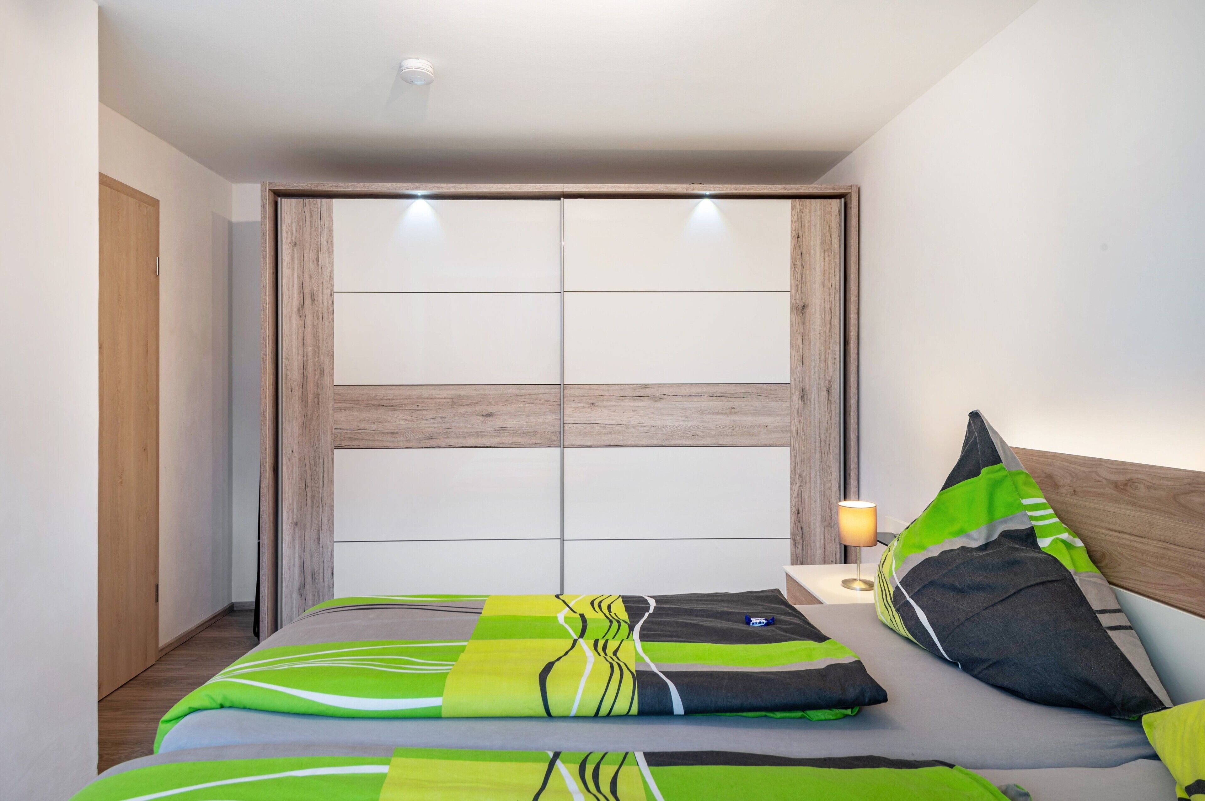 Een slaapkamer met een bed, kussens, een nachtkastje met lamp en een houten hoofdbord.