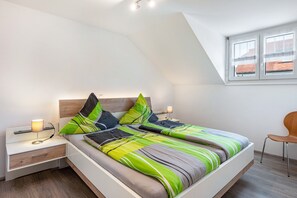 Une chambre à coucher moderne avec un plafond en pente, un grand lit avec une literie à rayures, des lampes de chevet et une table de chevet en bois.
