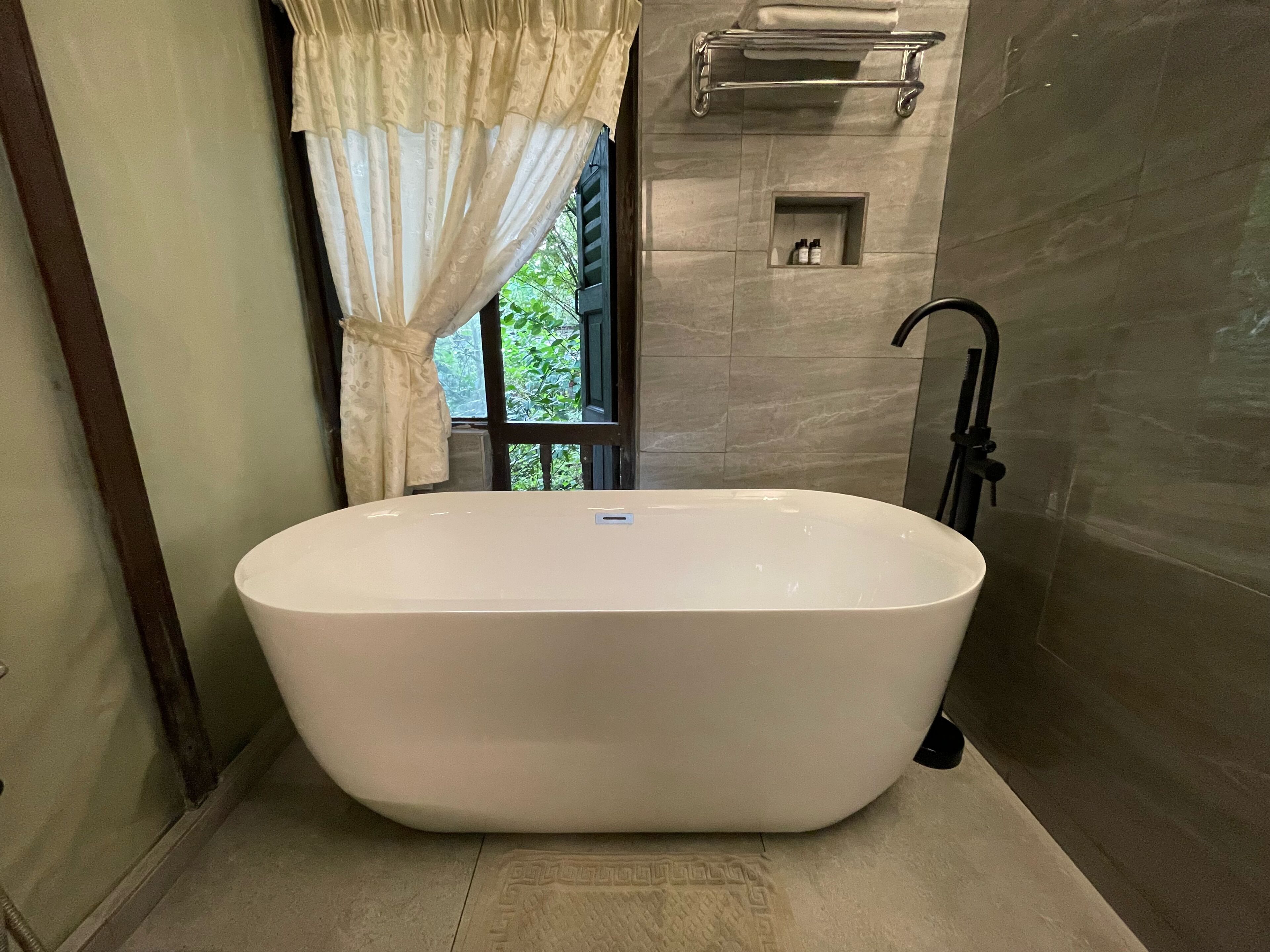 A modern bathroom with a freestanding bathtub, a towel rack, and a small shelf with toiletries.