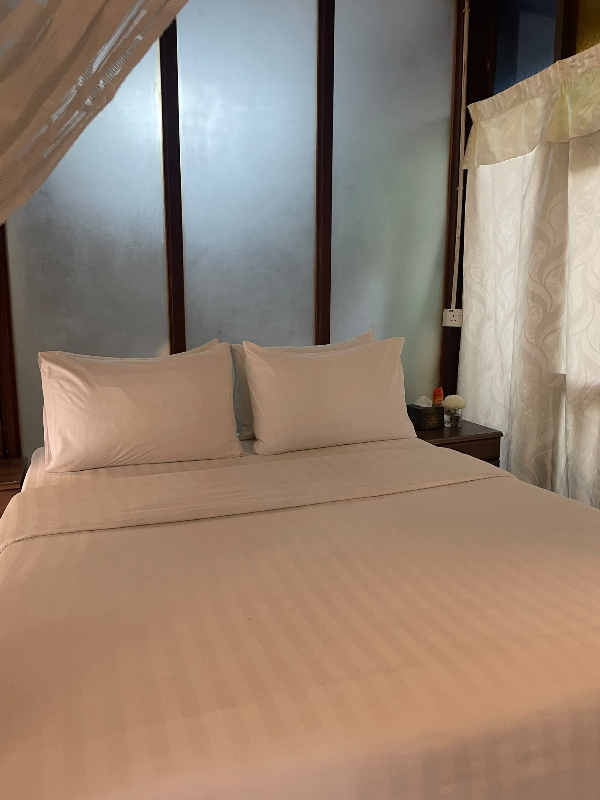 A bed with white linens in a room with a wooden headboard and a nightstand with a lamp.