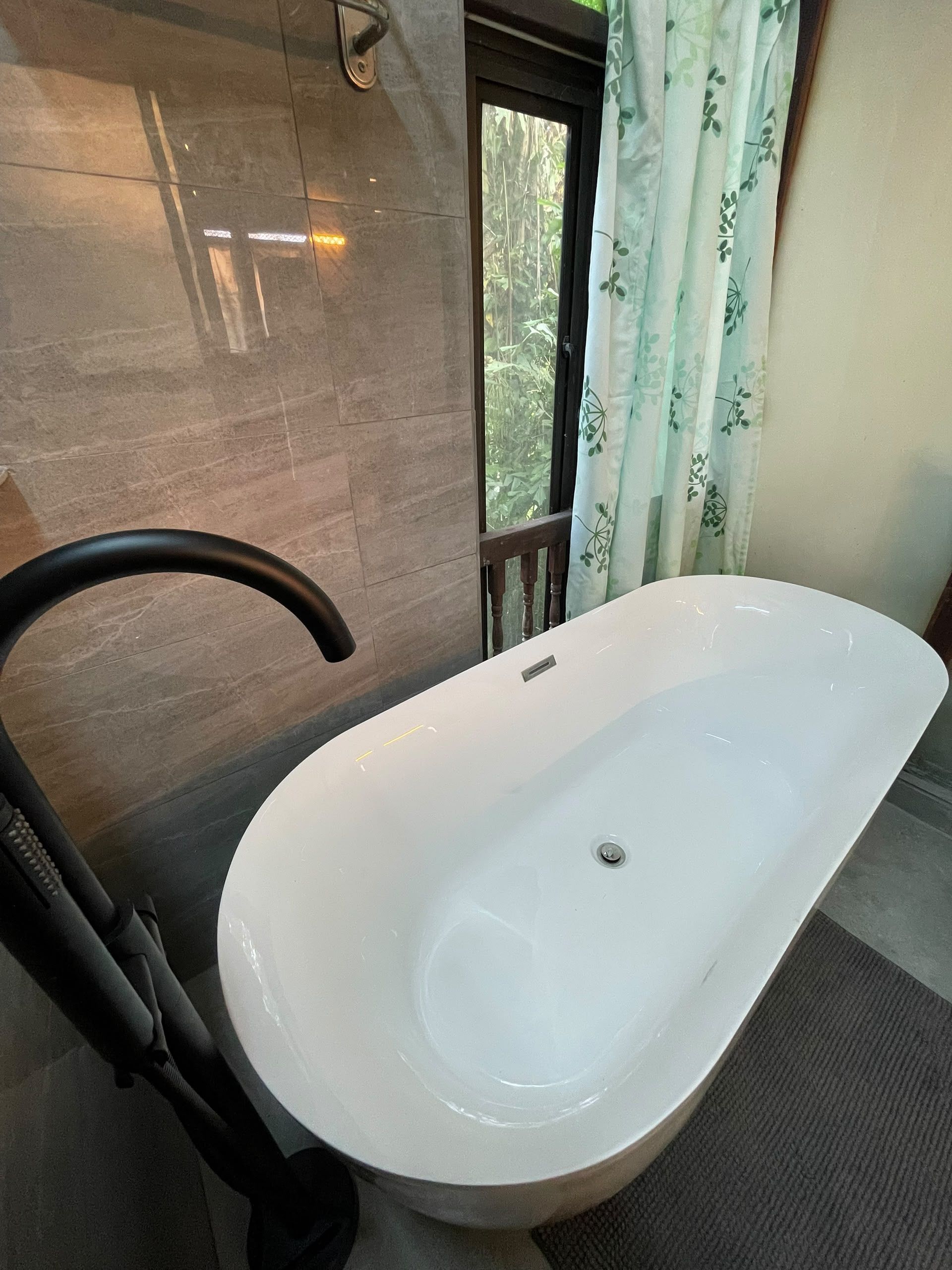 A bathroom with a white bathtub, a towel rack, and a window with curtains.
