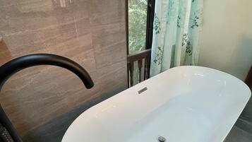 A bathroom with a white bathtub, a towel rack, and a window with curtains.