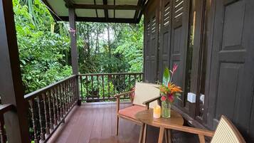 A covered porch with a wooden table and chairs, a candle, and a vase with flowers.