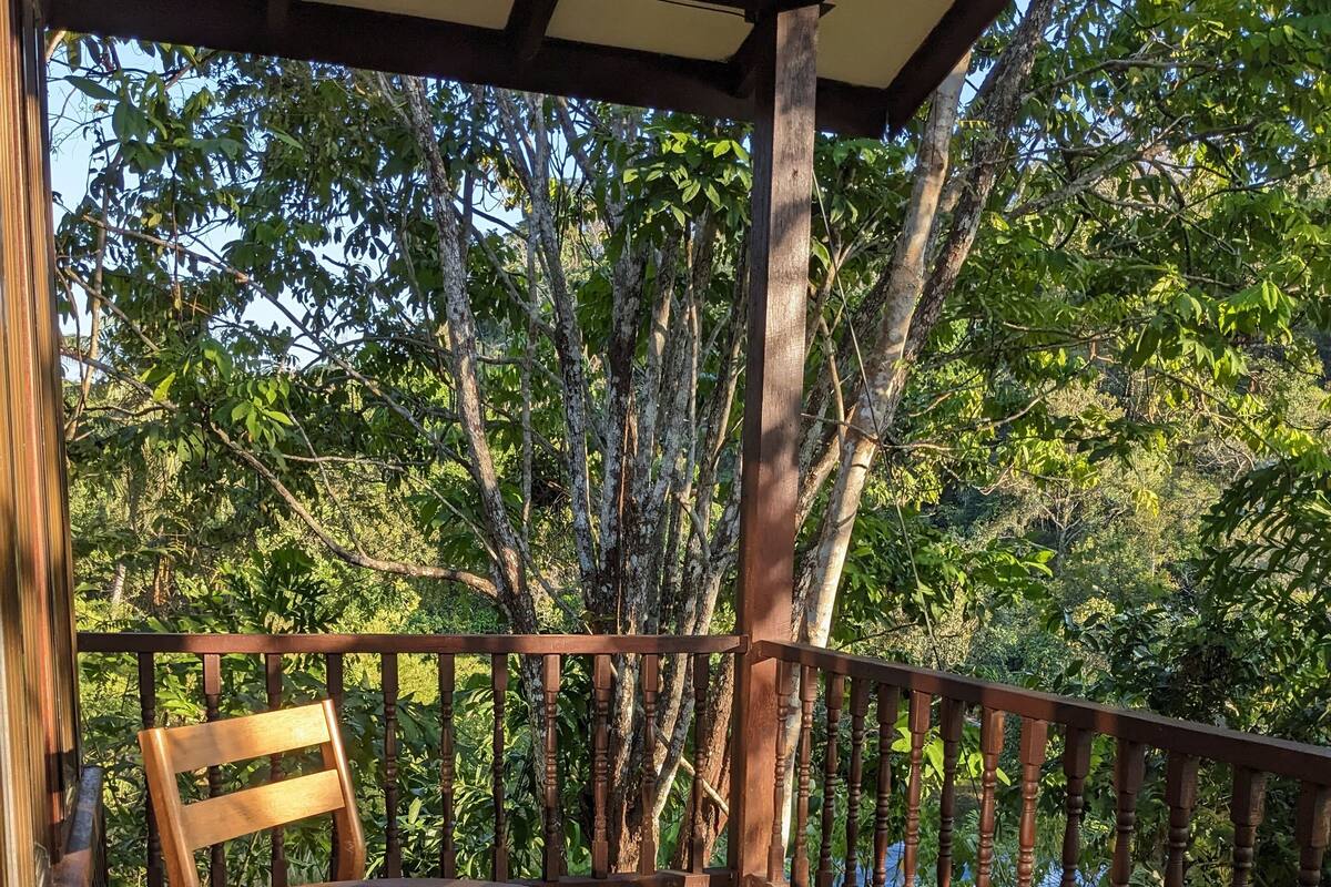 A wooden deck with a round table and two chairs, surrounded by a wooden railing, overlooking a lush green landscape.