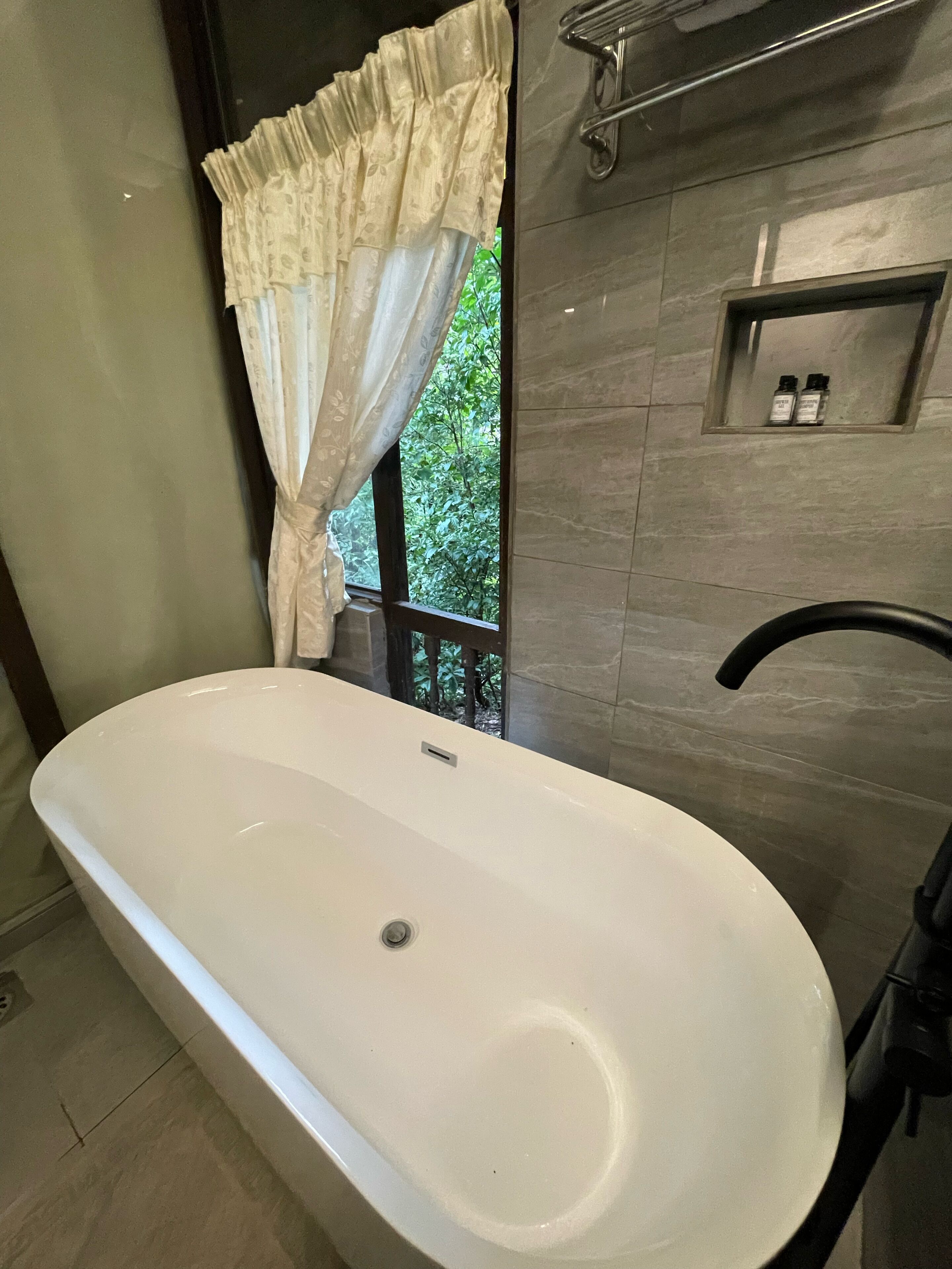 A bathroom with a freestanding bathtub, a window with a curtain, and a towel rack.