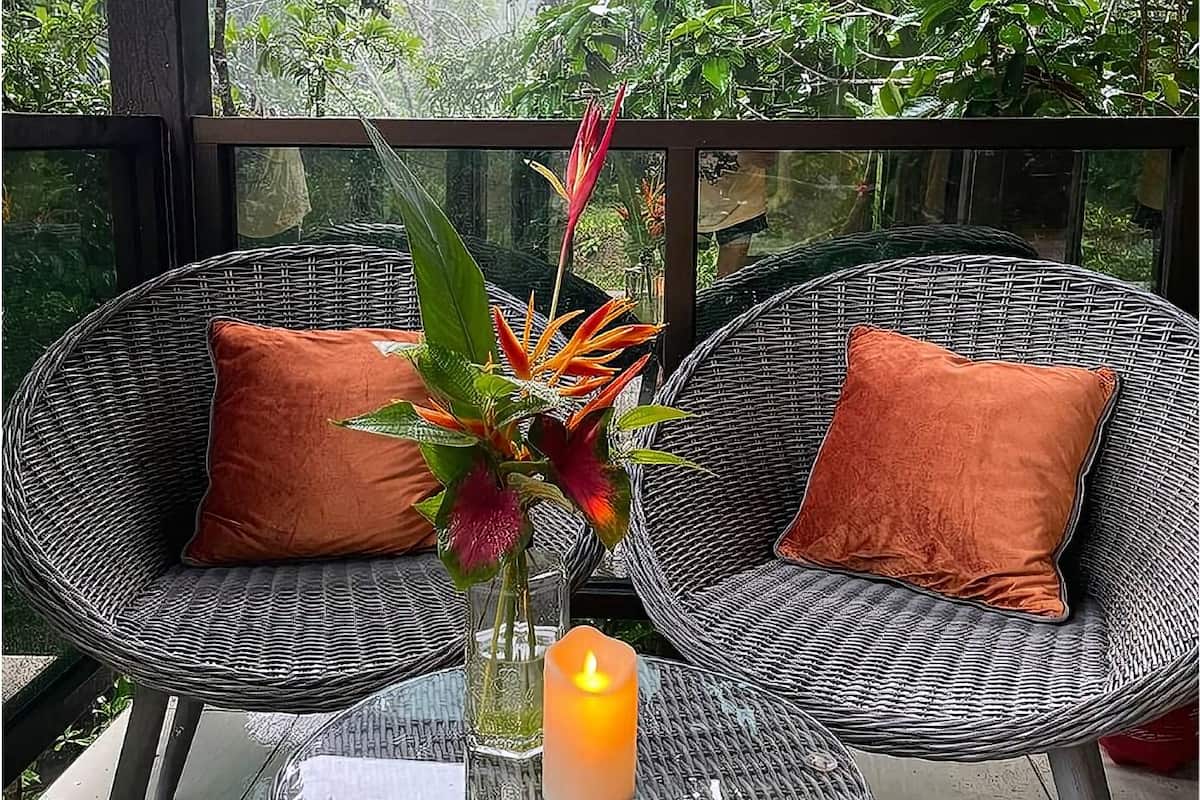 A wicker outdoor seating area with two chairs and a glass table, featuring a candle and a plant arrangement.