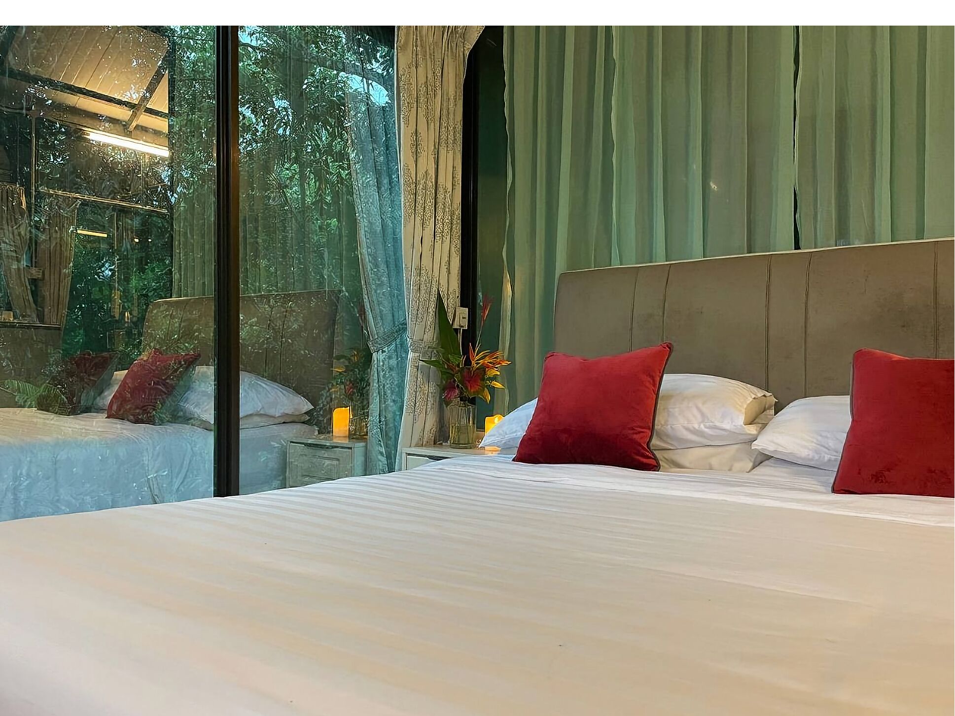 Ein Schlafzimmer mit einem großen Bett, einem Nachttisch, einer Blumenvase und Blick auf Grün durch ein Fenster.
