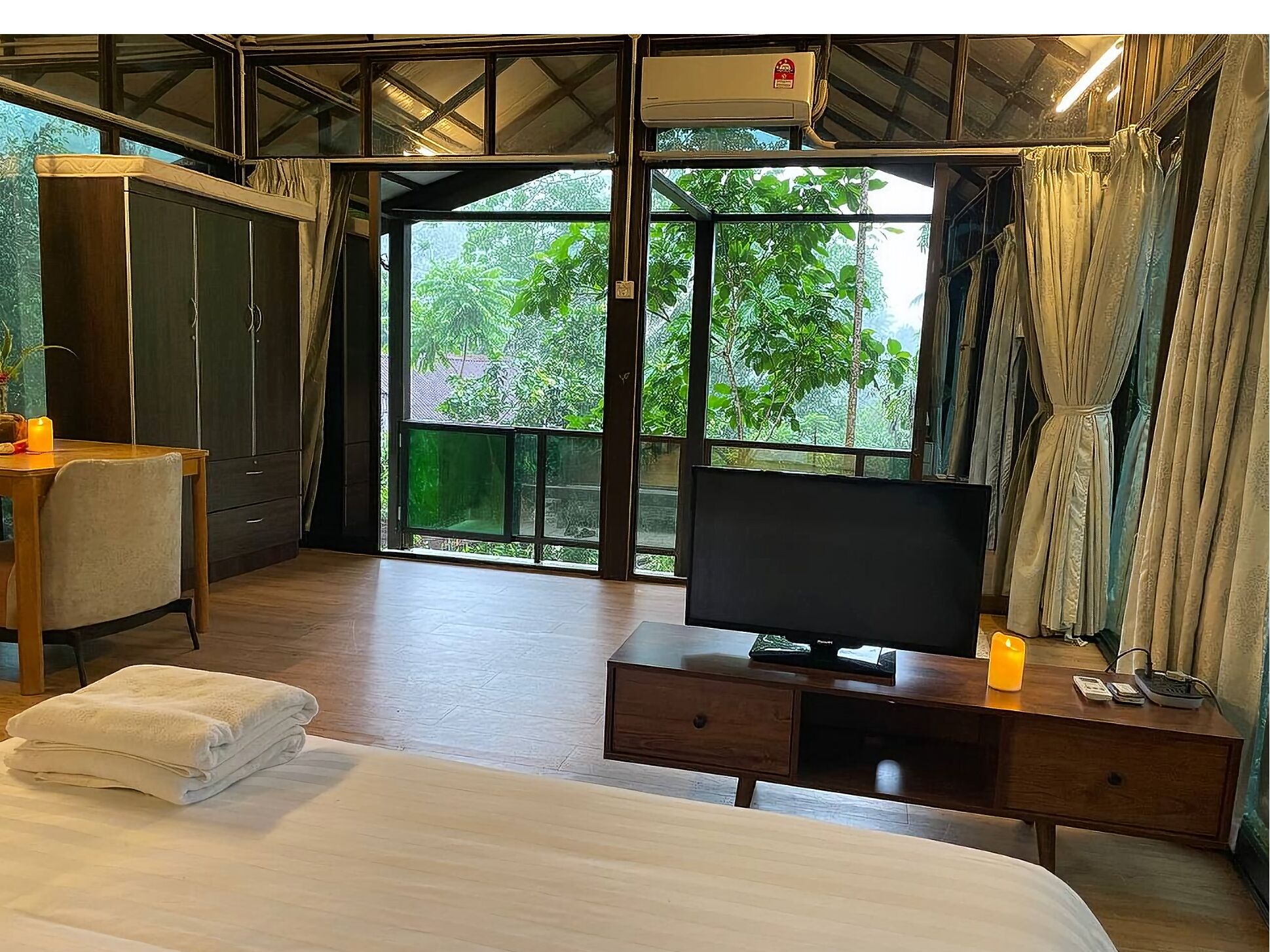 A hotel room with a bed, a desk with a TV, a wardrobe, and a large window with curtains.
