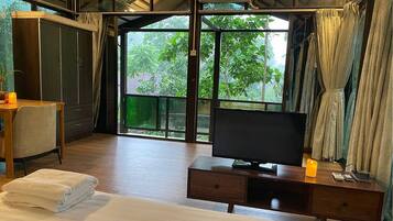 A hotel room with a bed, a desk with a TV, a wardrobe, and a large window with curtains.