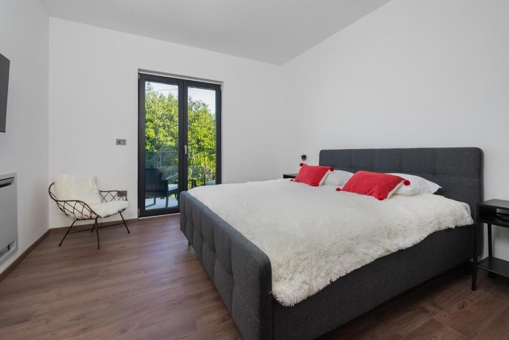 A modern bedroom with a large bed, a chair, and a sliding glass door leading to a balcony.