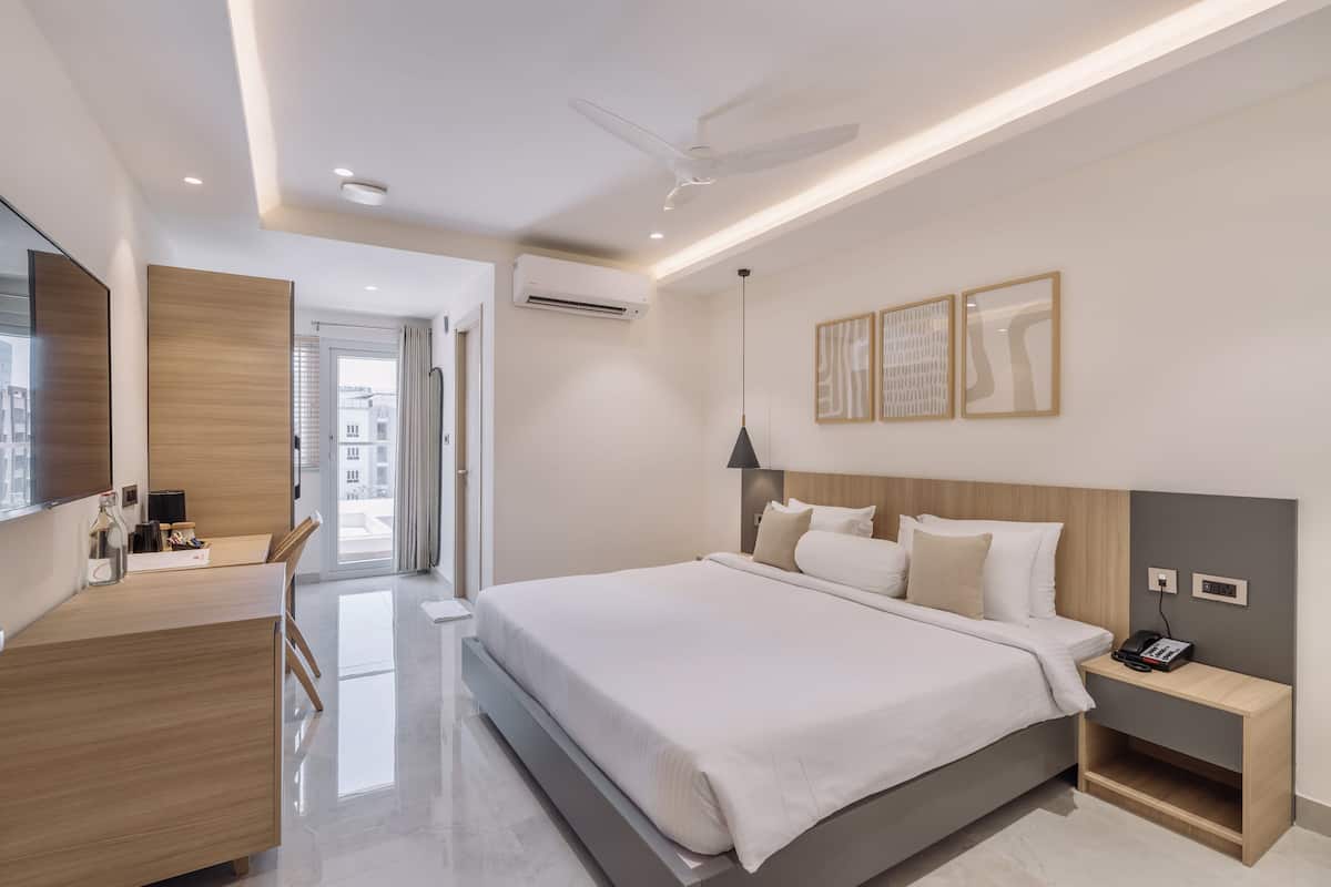 Une chambre d’hôtel moderne avec un grand lit, un bureau et une chaise. On y trouve un ventilateur de plafond, un appareil de climatisation et une table de chevet avec un téléphone.