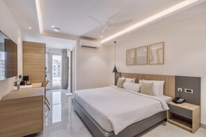Une chambre d’hôtel moderne avec un grand lit, un bureau et une chaise. On y trouve un ventilateur de plafond, un appareil de climatisation et une table de chevet avec un téléphone.