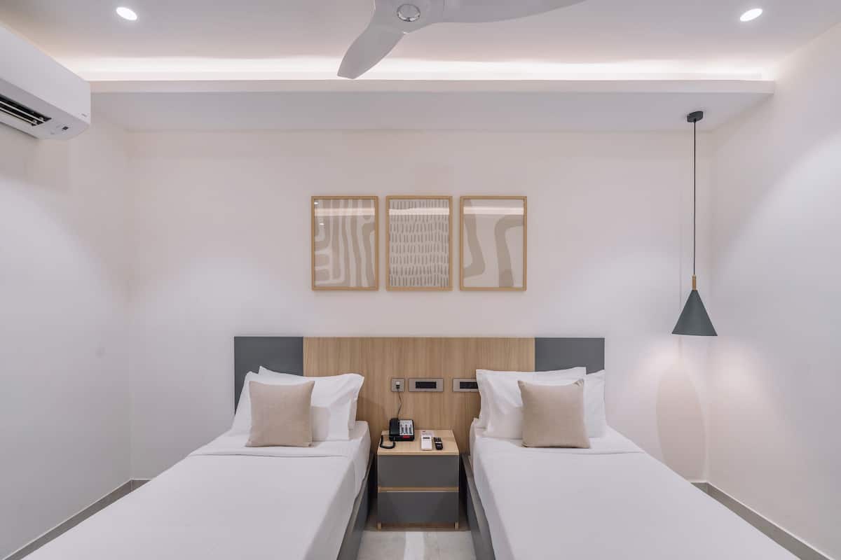 Une chambre d’hôtel avec deux lits, une tête de lit en bois, une table de chevet avec un téléphone et un ventilateur de plafond.