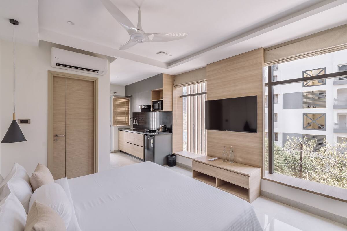 Une chambre d’hôtel moderne équipée d’un grand lit, d’une télévision, d’un ventilateur de plafond et d’une kitchenette.