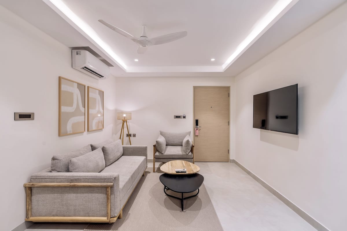 Un salon moderne comprenant un canapé, un fauteuil, une table basse, un ventilateur de plafond, un téléviseur fixé au mur et des œuvres d’art accrochées au mur.