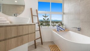 Un baño moderno con un ventanal grande, un tocador de madera, una bañera y una zona de ducha.
