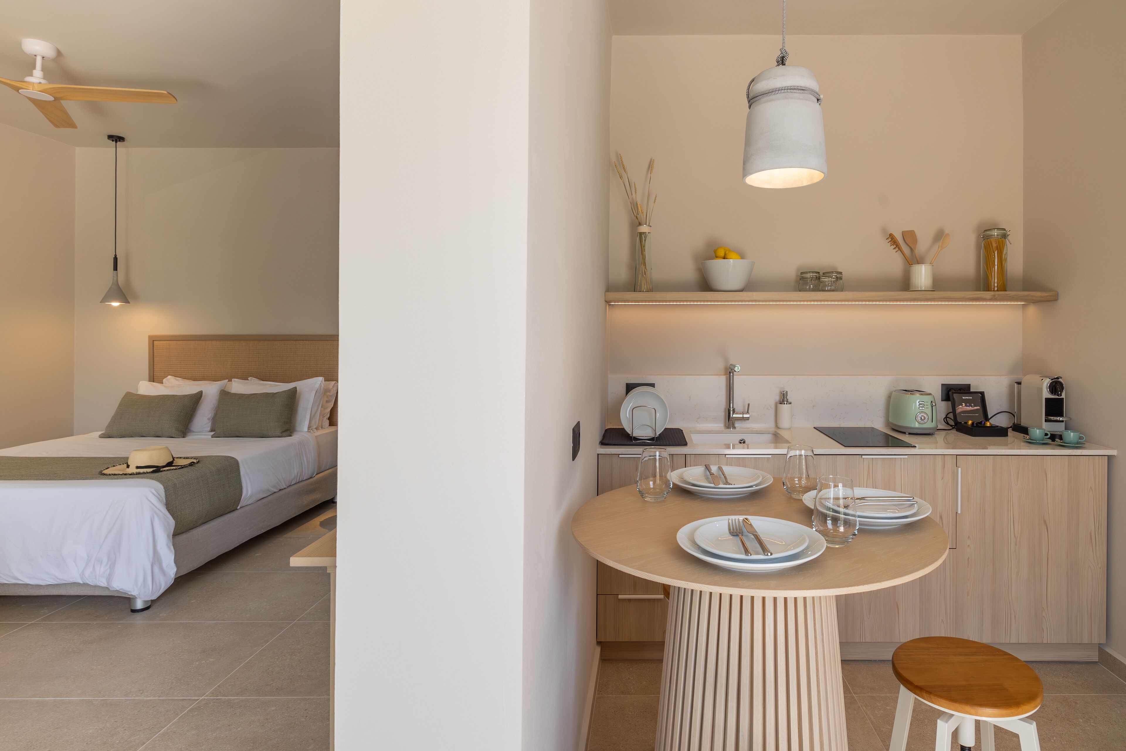 A modern hotel room with a bed, bedside table, and a small kitchenette.