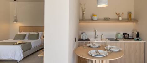 A modern hotel room with a bed, bedside table, and a small kitchenette.