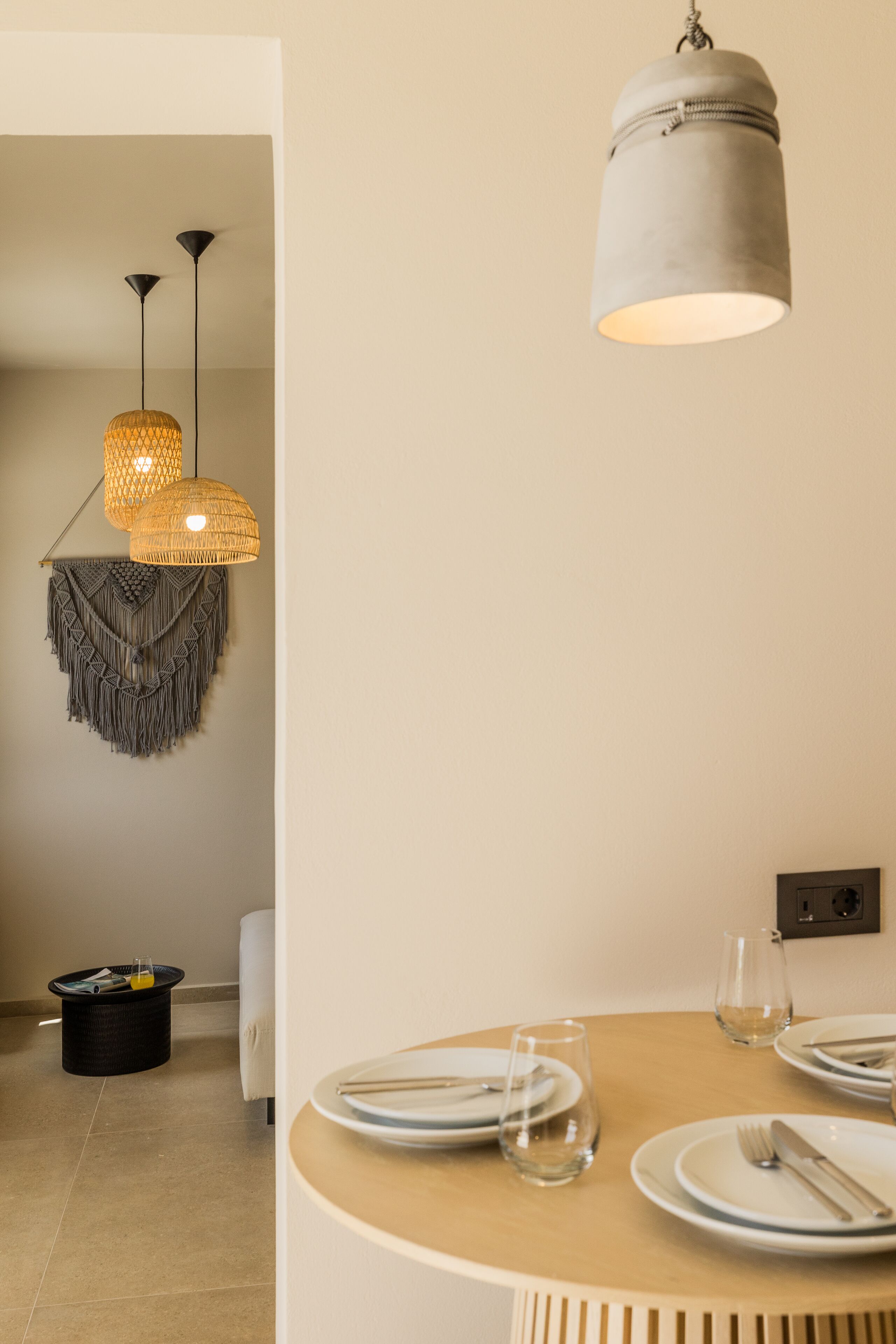 Un comedor con una mesa redonda dispuesta para dos personas, una lámpara colgante y un enchufe en la pared.