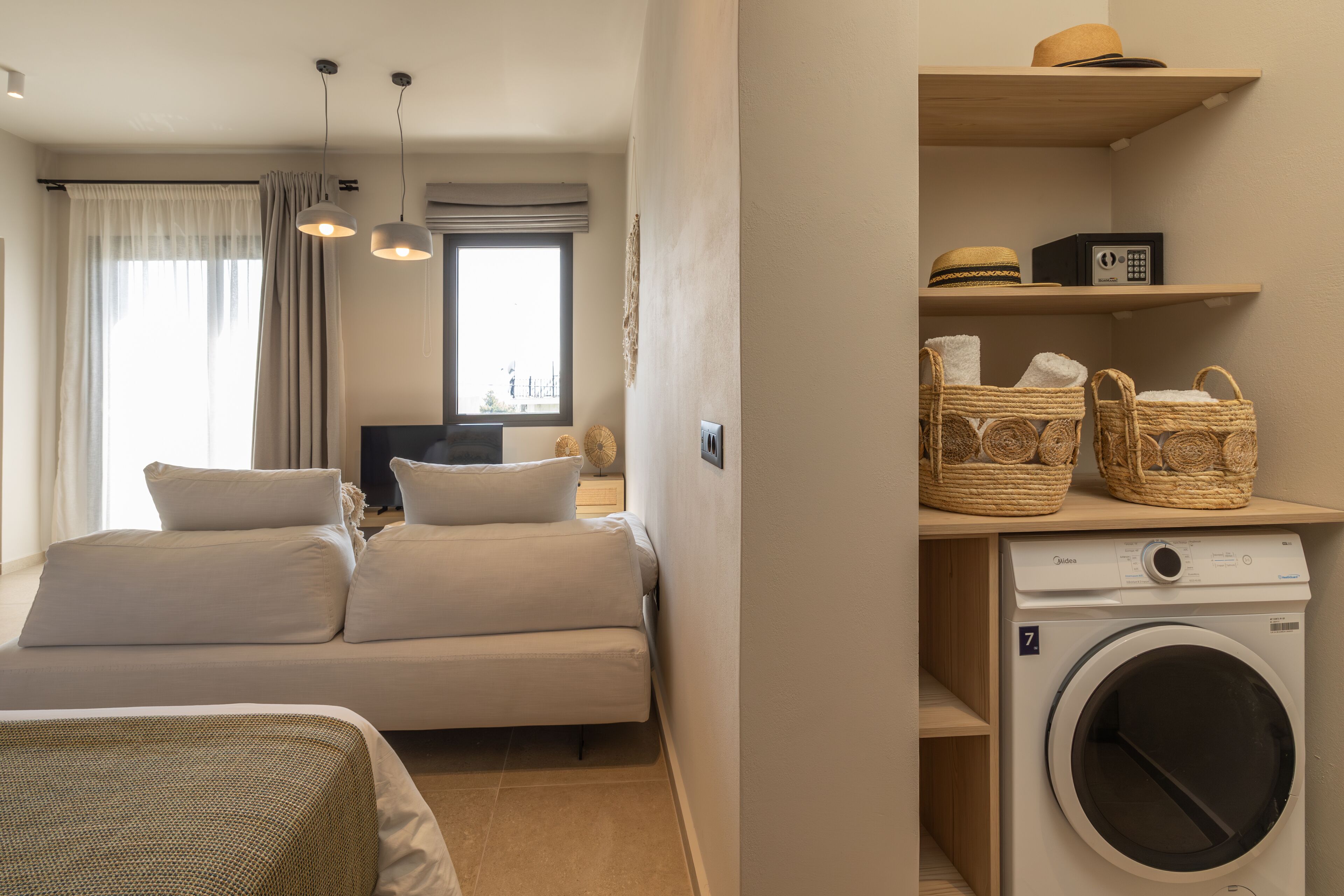 Ein kompakter Wohnraum mit Sofa, Waschmaschine und einem fenster mit Vorhängen.
