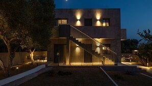 A modern building with a staircase leading to the upper floor, surrounded by trees and a well-lit outdoor area. - Topos Suites (Kefalonia)
