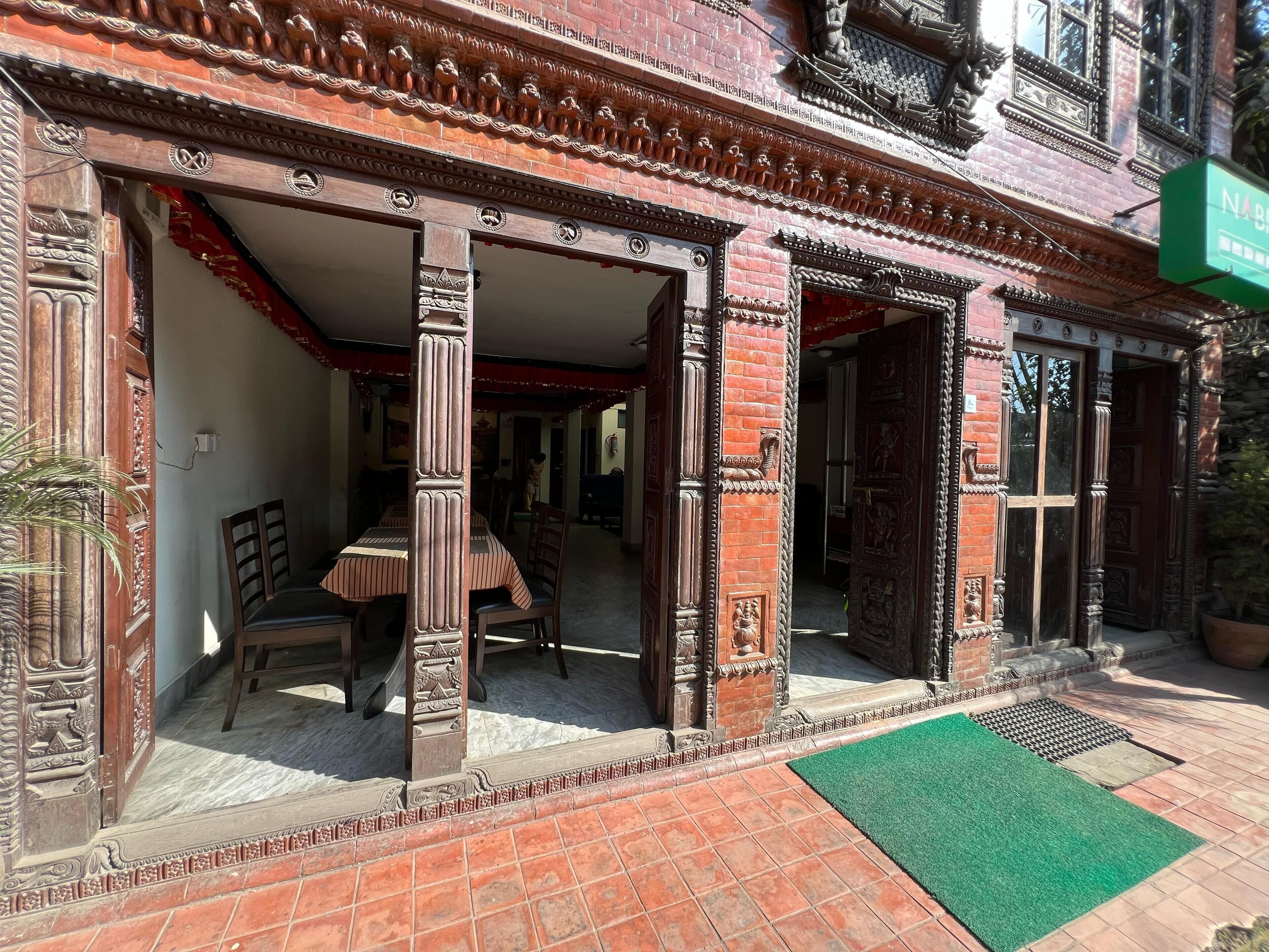 A traditional building with ornate wooden doors and columns, a tiled patio, and a green mat.