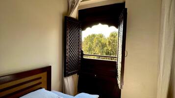 A bedroom with a bed, a window with curtains, and a view of trees outside.