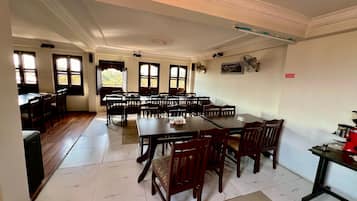 A spacious dining area with multiple tables and chairs, large windows with views, and a ceiling fan.