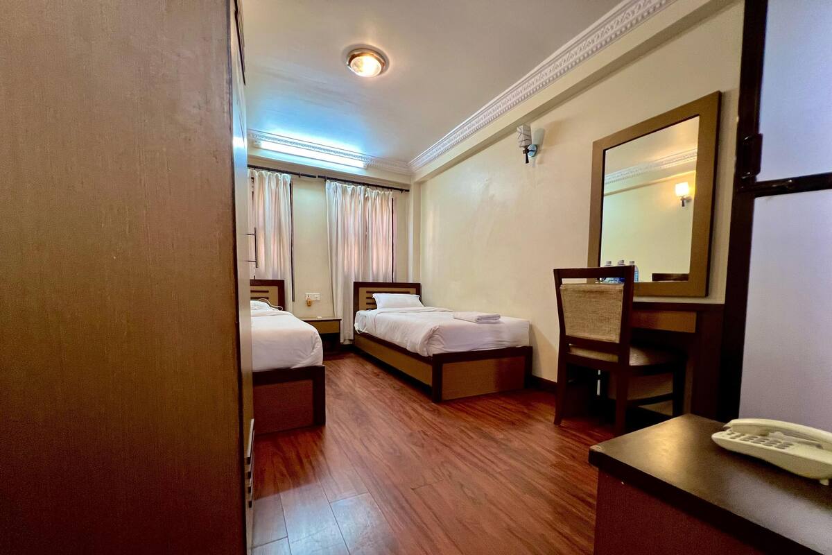 A hotel room with two beds, a desk with a telephone, and a mirror.