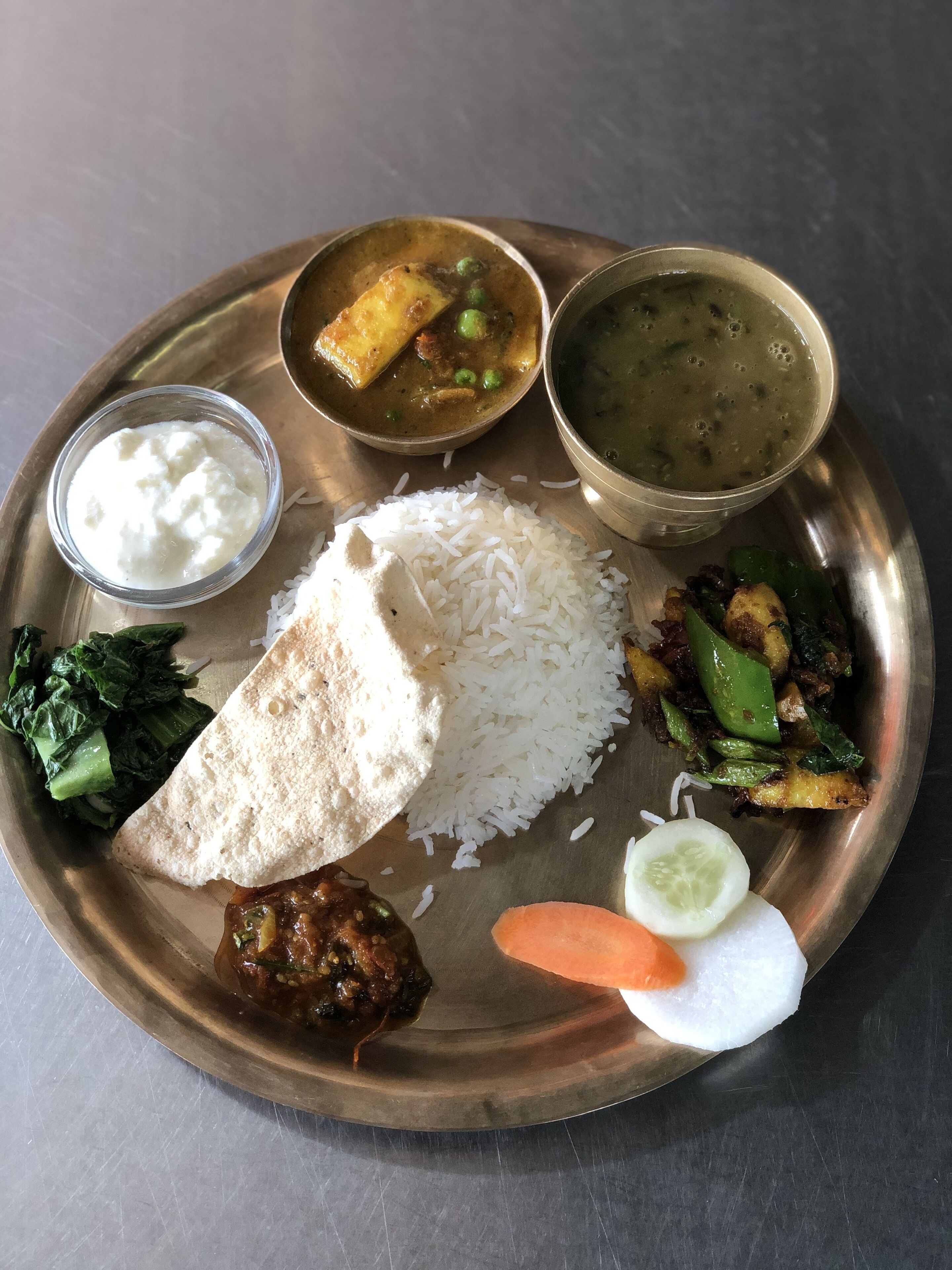 A traditional Indian meal on a metal plate, including rice, paneer, mixed vegetables, and two types of curry.