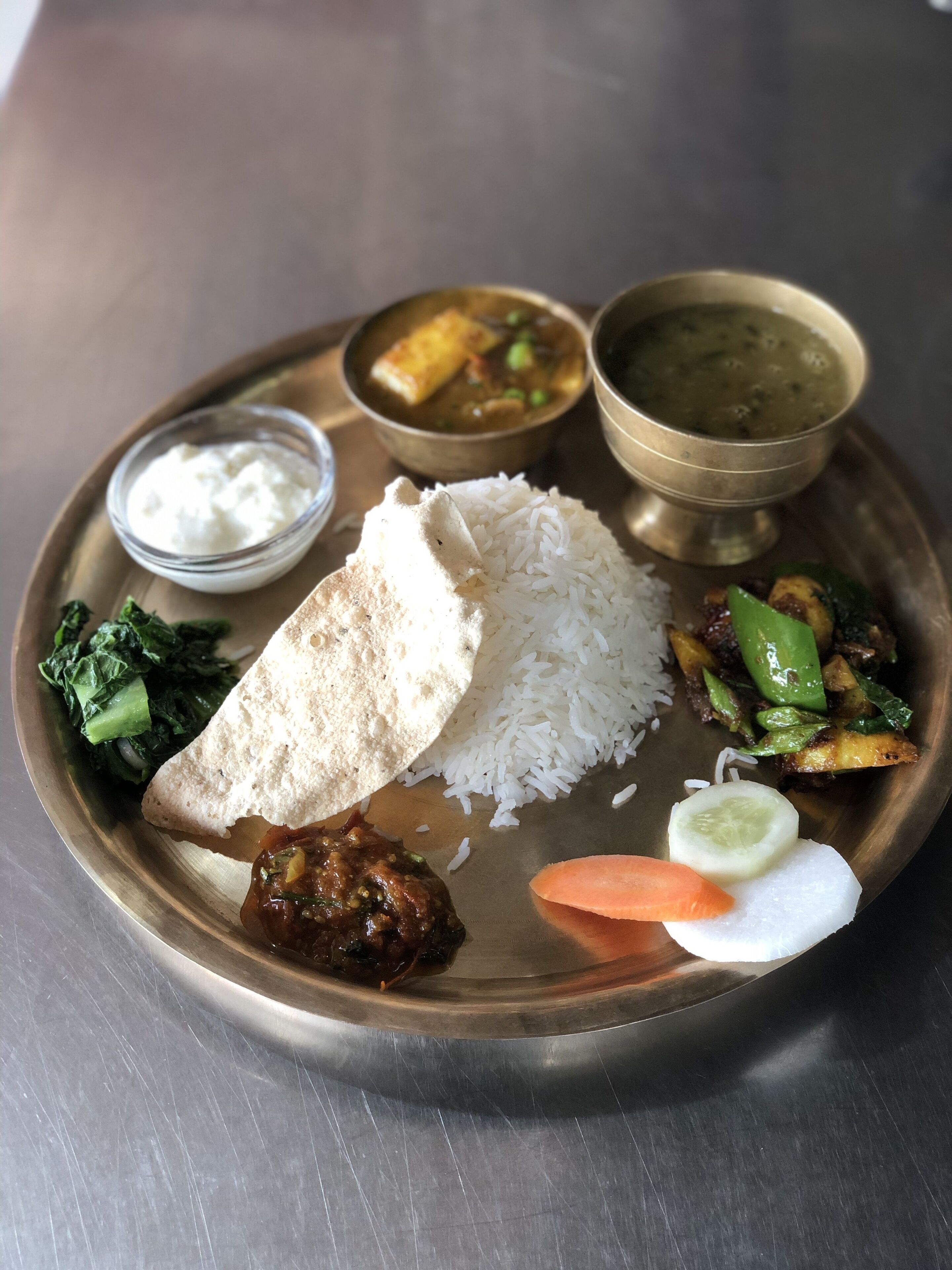 A meal with rice, flatbread, vegetables, and two types of curry on a metal plate.